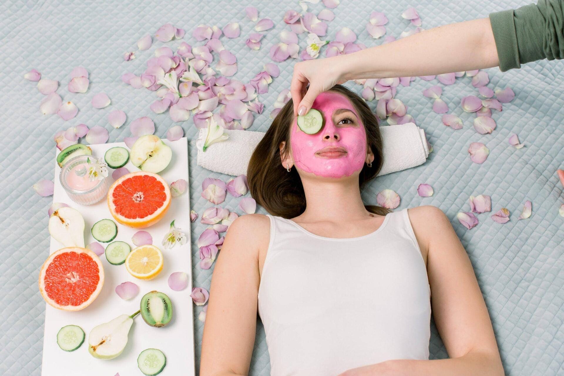 beautiful young woman receiving spa treatment with pink cosmetic mask, and slices of cucumber on her eyes, skincare, antiaging, acne