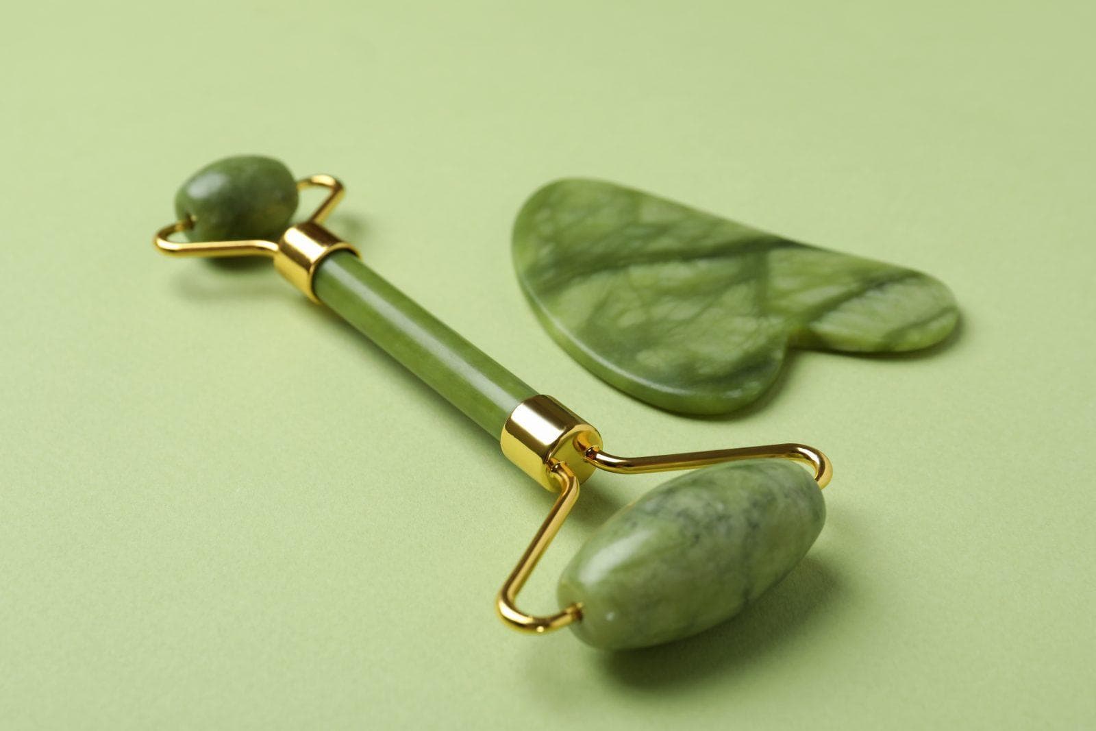 face roller and gua sha on green background