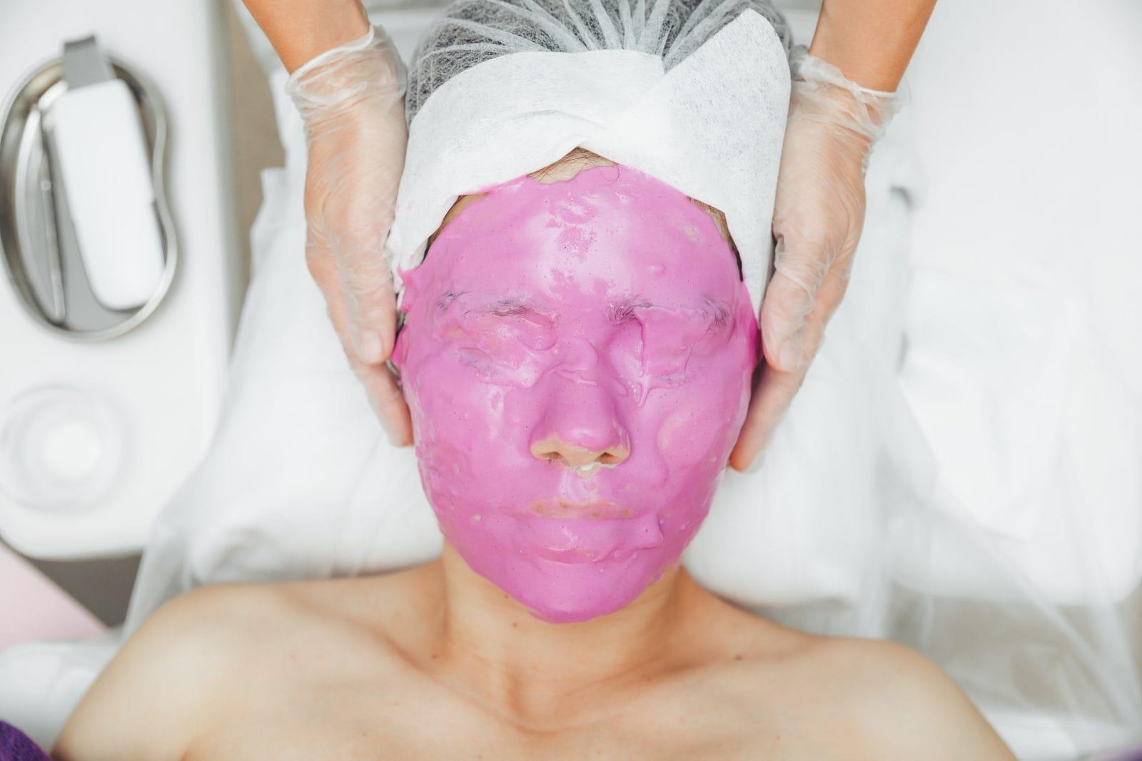 care for the beauty of women's skin. a young woman with an alginate cosmetic purple mask on her face skin in a beauty salon.