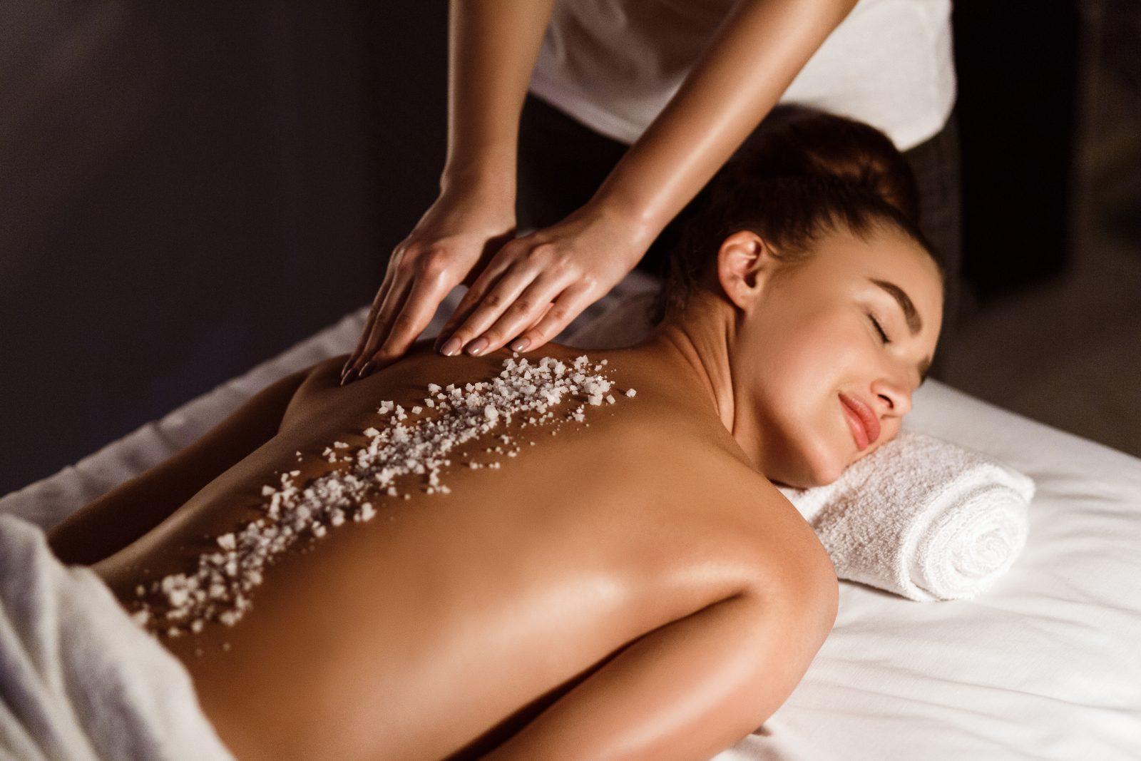 woman enjoying salt scrub massage, relaxing in health spa