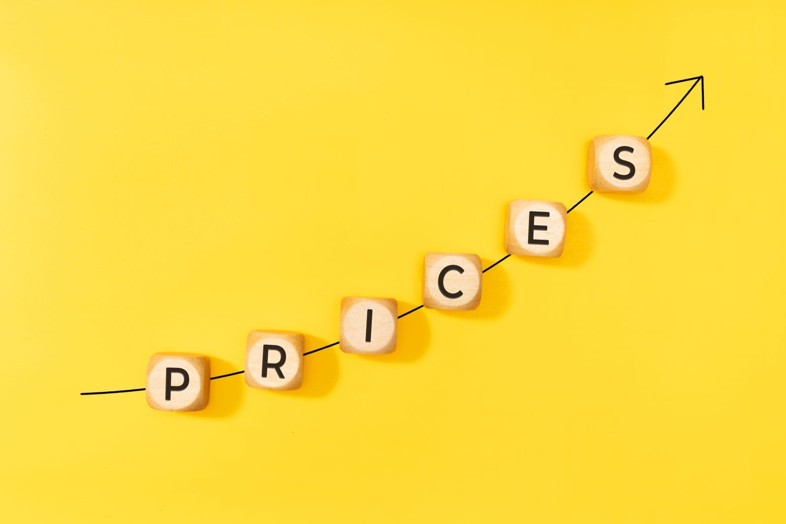 rising prices concept. rising arrow and text on wooden blocks on yellow background. copy space