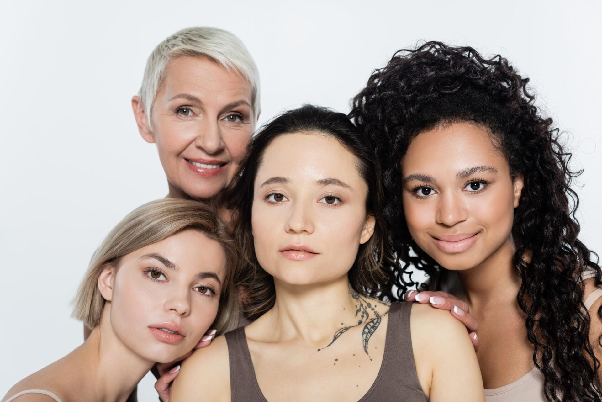 smiling interracial women hugging tattooed friend isolated on grey, feminism concept